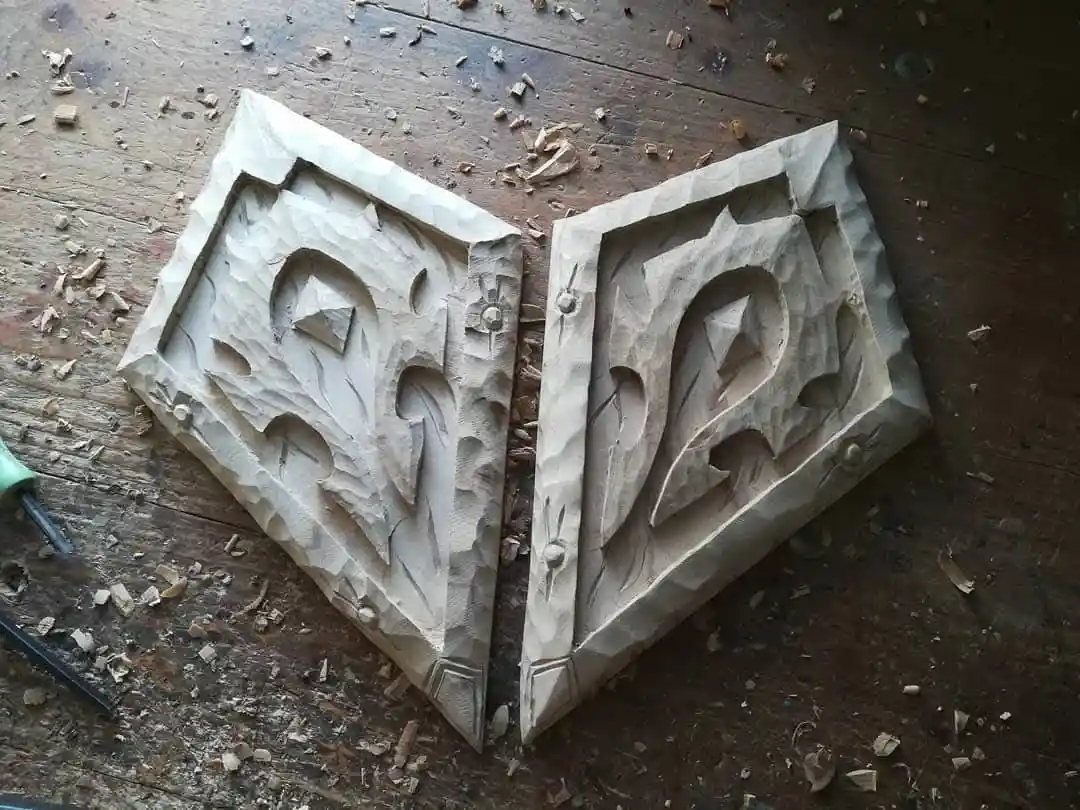 Two roughly carved wooden plaques shaped like the letters 'R' and 'A' lie on a workbench covered in wood shavings. The…