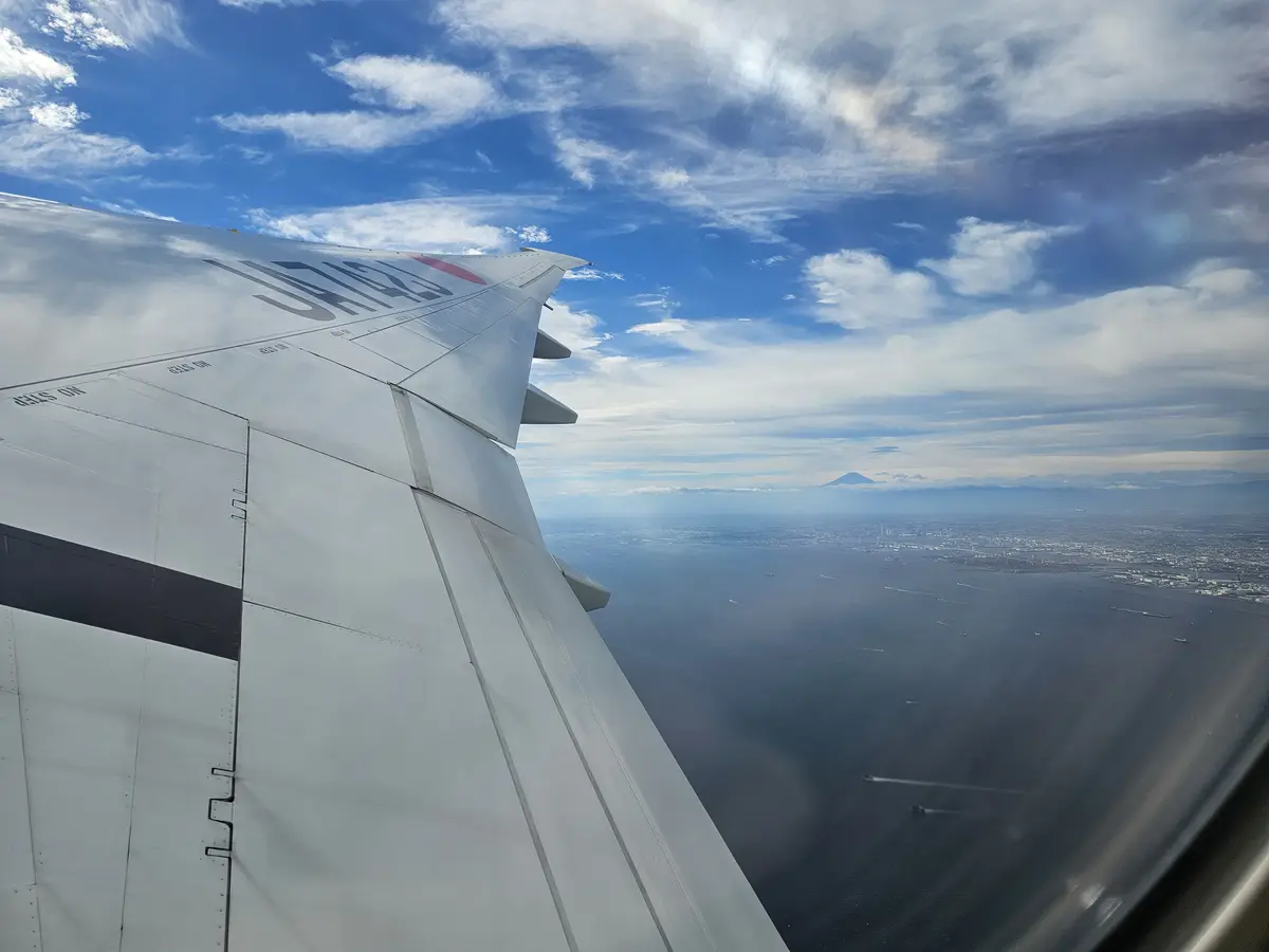 A view from an airplane window showing the wing with 'UNITED' branding against a blue sky with clouds, overlooking a large…