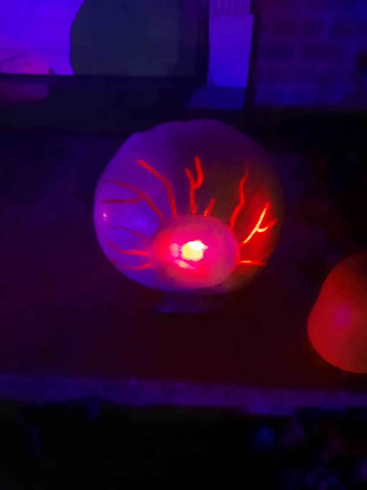 A carved pumpkin illuminated from within, glowing with red veins and a bright yellow center, set against a dark purple-lit…