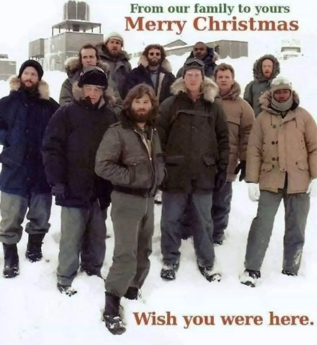 A group of men in heavy winter coats and hats stand in a snowy outdoor setting, looking at the camera. The image has…
