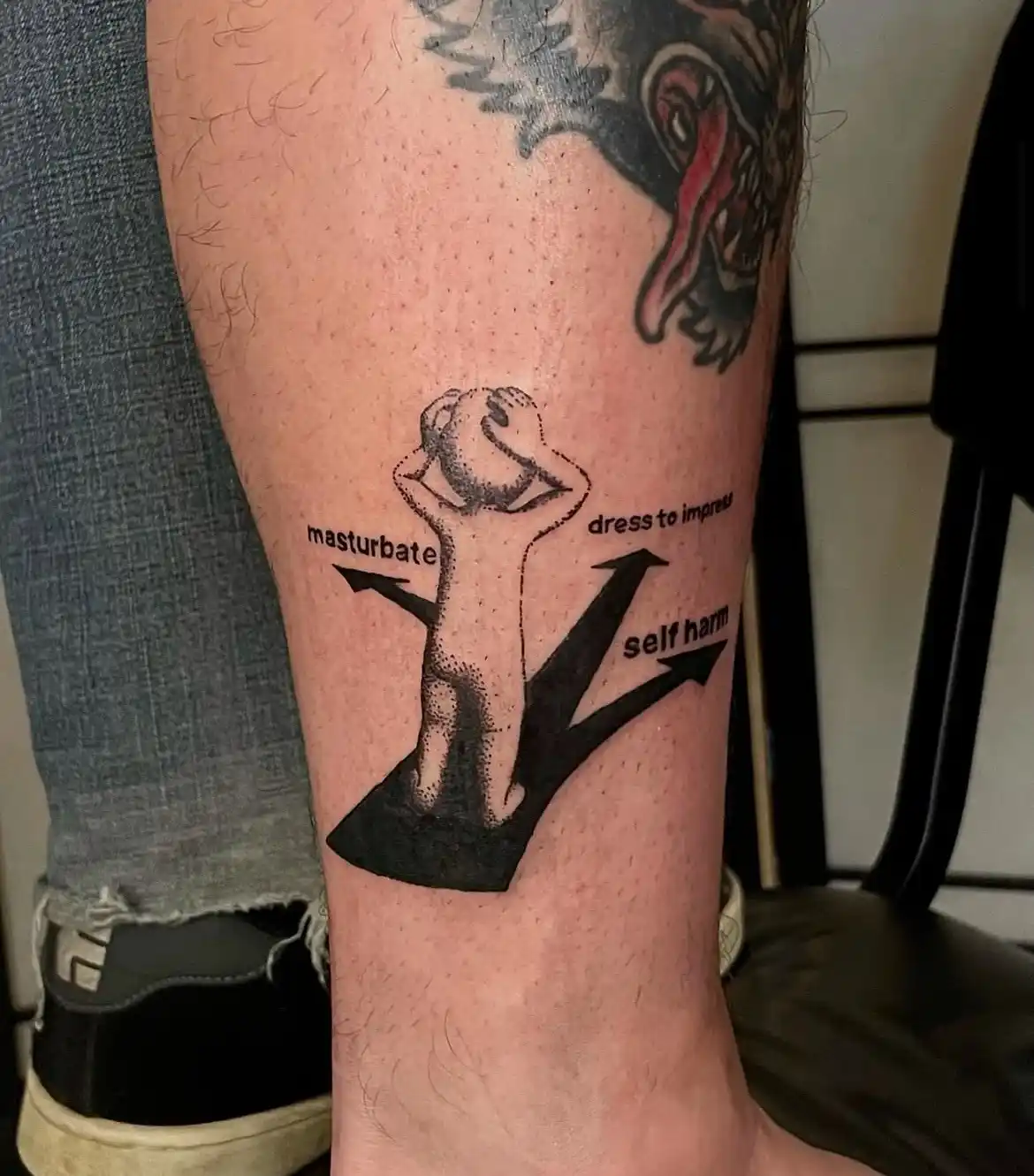 A close-up photo shows a tattoo on a person's lower leg featuring a stylized figure standing on a black arrowhead with three…
