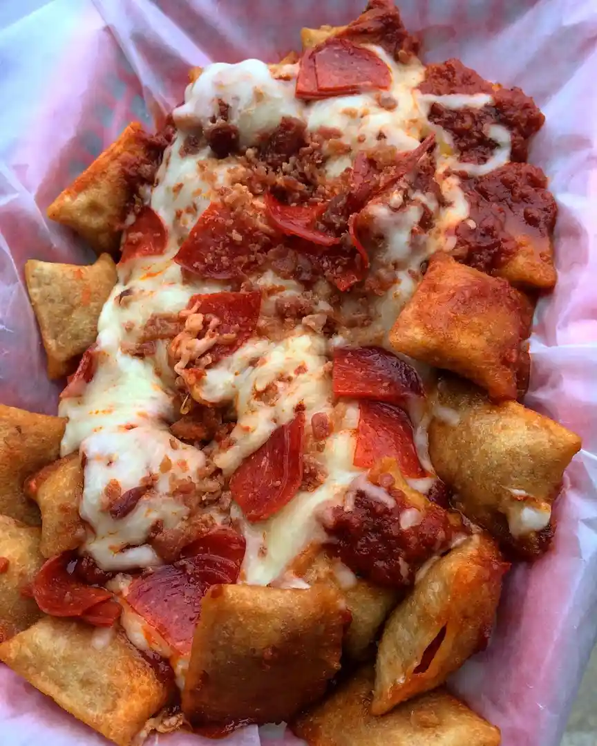 a close-up photo of a basket filled with fried, square-shaped dough pieces topped with melted white cheese, red pepperoni…