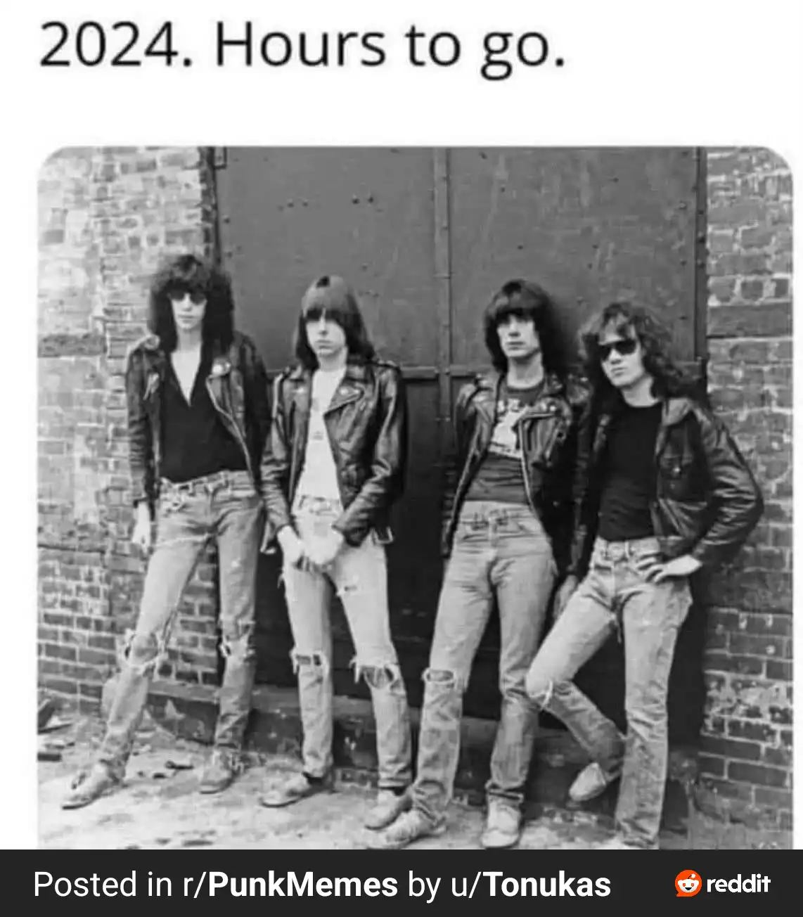 A black-and-white photo shows four young men in 1970s punk rock style, wearing leather jackets and ripped jeans, standing…