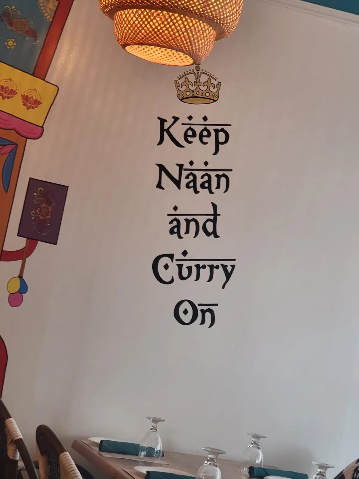 A wall in a restaurant features a decorative sign with a gold crown above the text 'Keep Naan and Curry On,' styled to mimic…