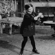 A black-and-white sequence of six frames shows a young girl in a dark coat and boots performing a dance or playful motion in…