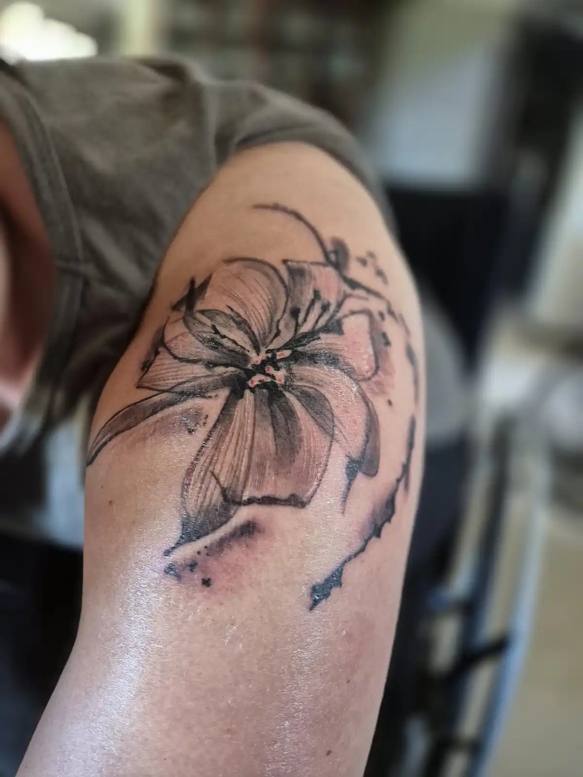 A close-up photo shows a freshly inked floral tattoo on a person's upper arm, featuring black outlines and pink shading with…