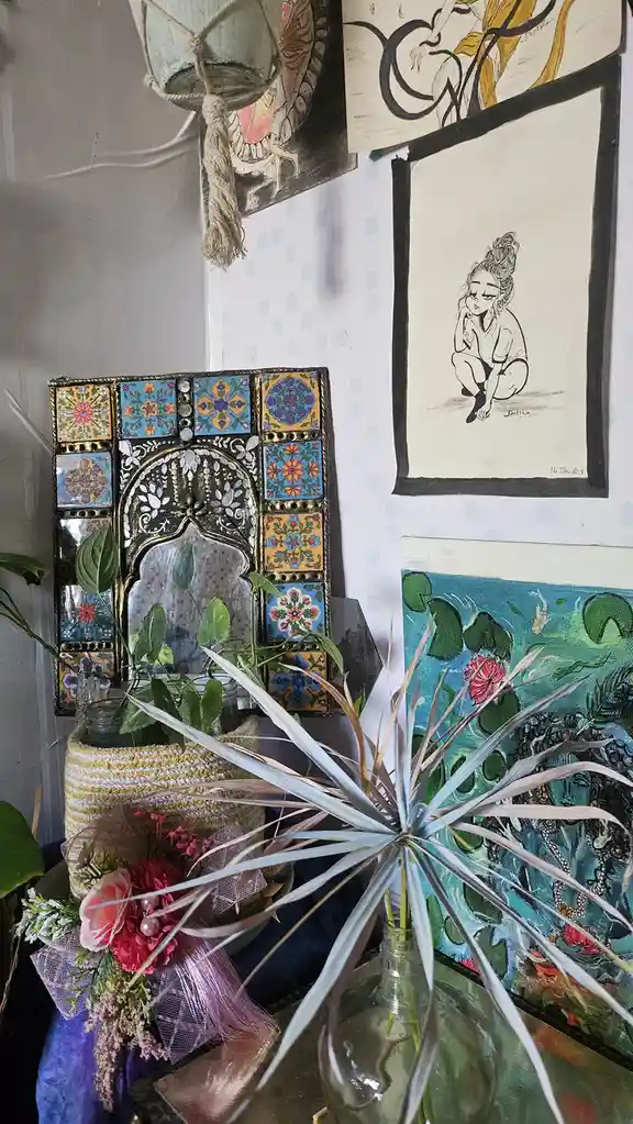 A cozy, eclectic room corner features a decorative tiled mirror with an arched frame, surrounded by various artworks…