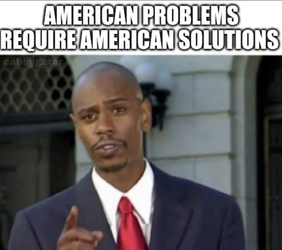 A man in a dark suit and red tie stands outdoors, pointing his finger forward with a serious expression. Large white text at…