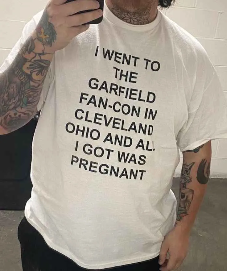 A person with tattoos on both arms is taking a selfie while wearing a white t-shirt that reads 'I WENT TO THE GARFIELD…