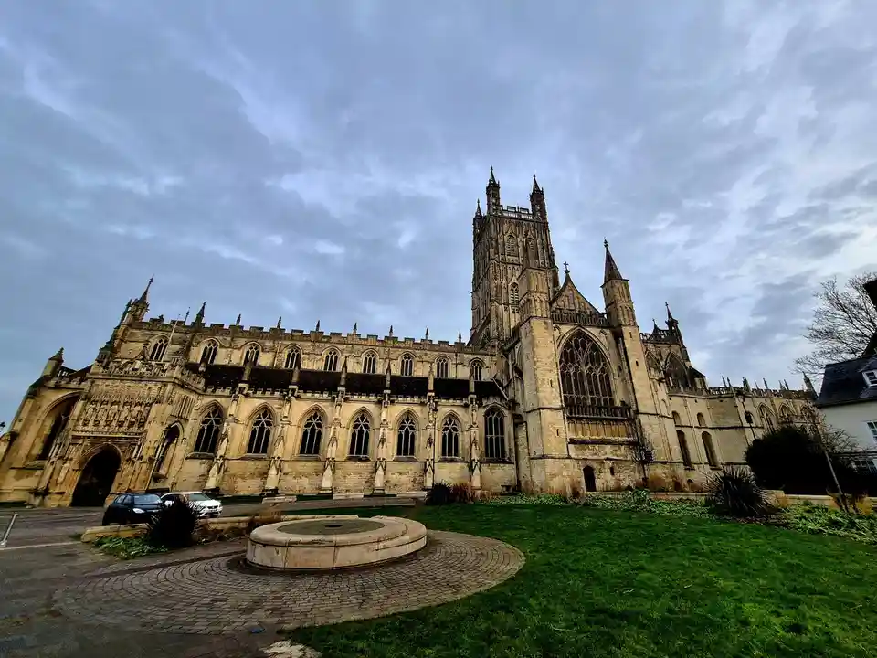 A low-angle photo shows a large, ornate Gothic cathedral with multiple spires and pointed arch windows under a cloudy sky…