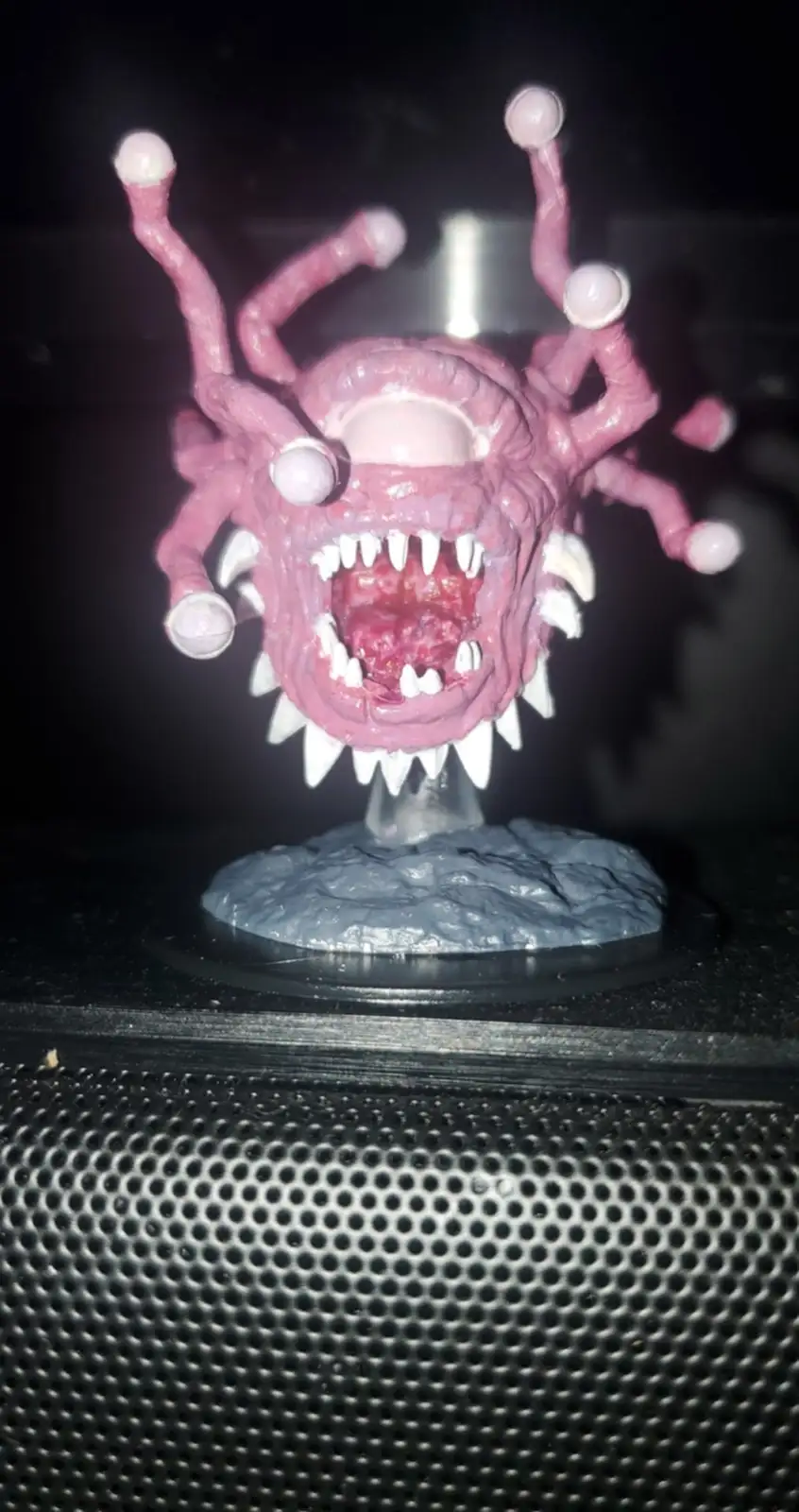 A pink, monstrous figurine with multiple tentacles tipped with eyeballs and a wide mouth full of sharp white teeth sits on a…