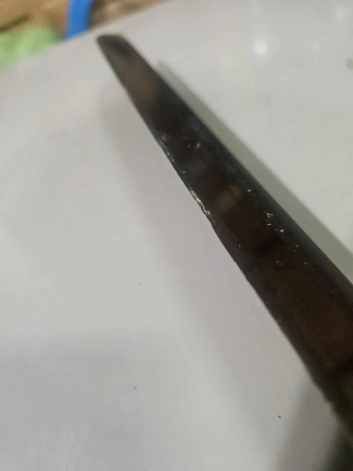 A close-up photo shows the dark, worn blade of a knife resting diagonally on a plain white surface, with visible scratches…