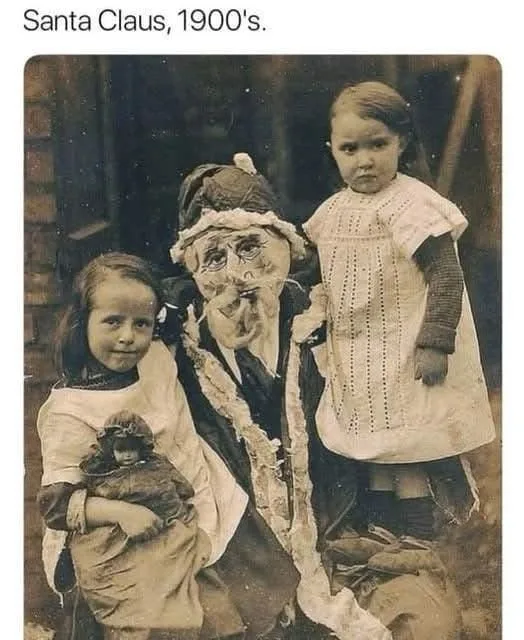A sepia-toned, vintage photograph from the 1900s shows a man dressed as Santa Claus with a very weathered, wrinkled face and…