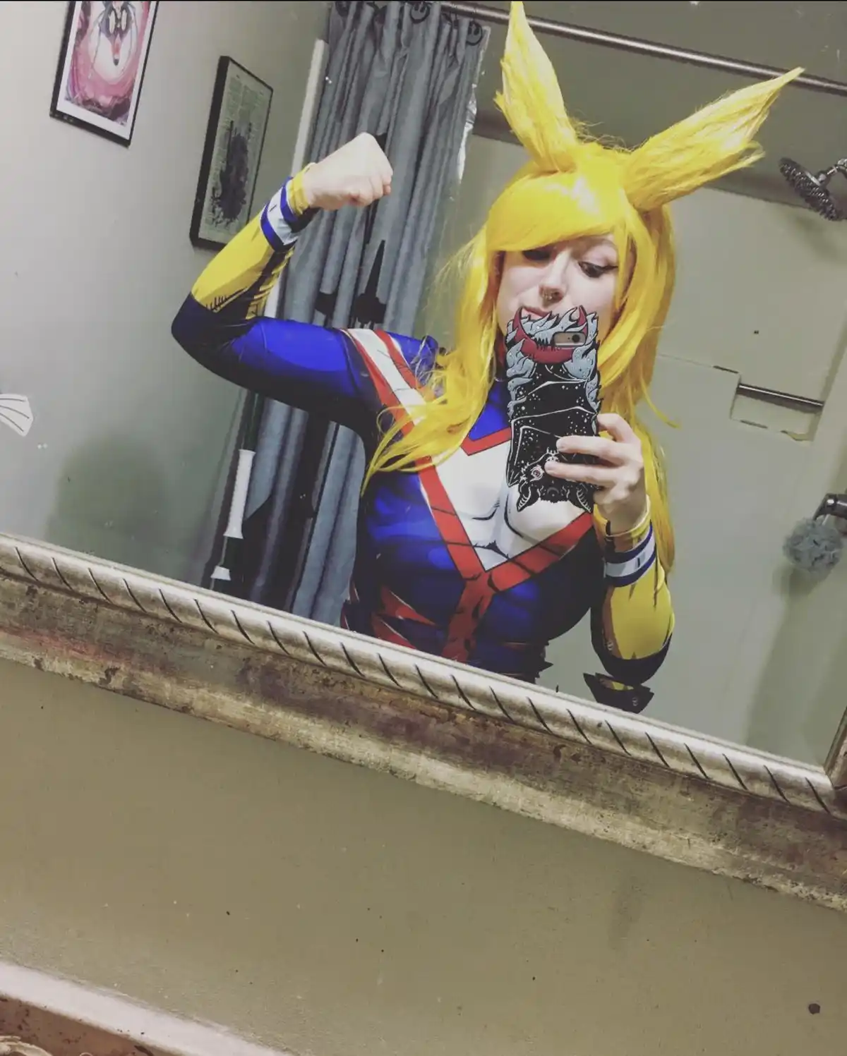 A person in a My Hero Academia cosplay of Momo Yaoyorozu takes a mirror selfie in a bathroom, flexing their bicep while…
