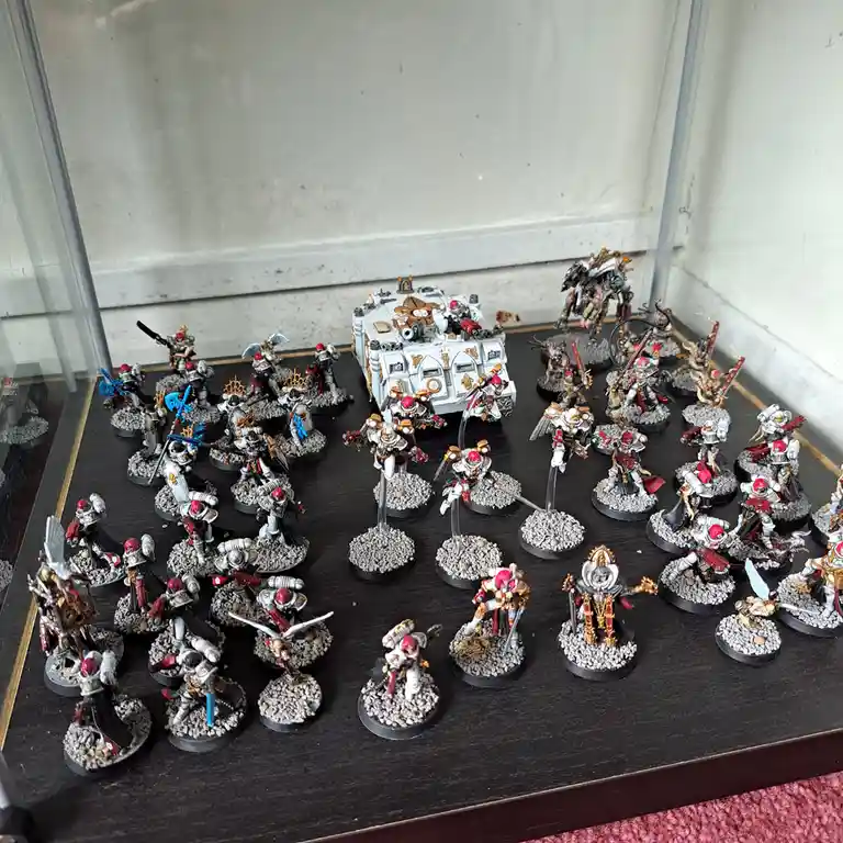 A glass display case holds dozens of intricately painted Warhammer 40,000 miniatures, including infantry, vehicles, and a…