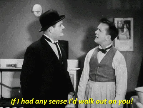 A black-and-white film still shows two men in a kitchen. The man on the left, wearing a hat and suit, says 'If I had any…