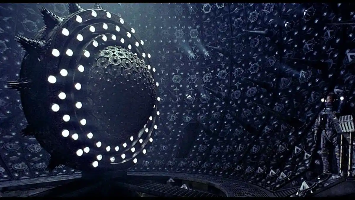 A dark, sci-fi scene from the movie 'Alien' shows a large, spiky, circular object with glowing white lights embedded in it…