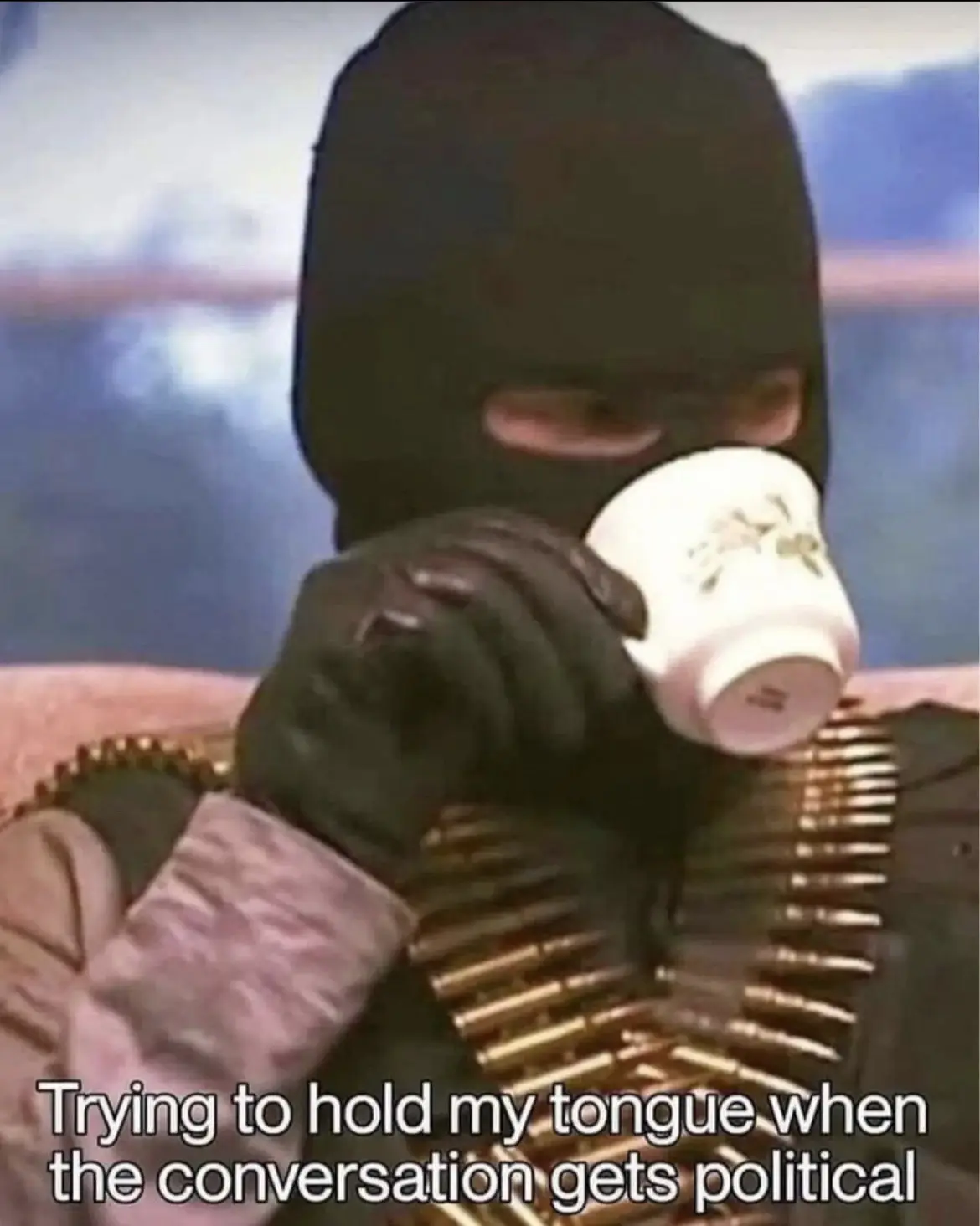 A person wearing a black balaclava and black gloves holds a white teacup to their mouth while wearing a bandolier of bullets…
