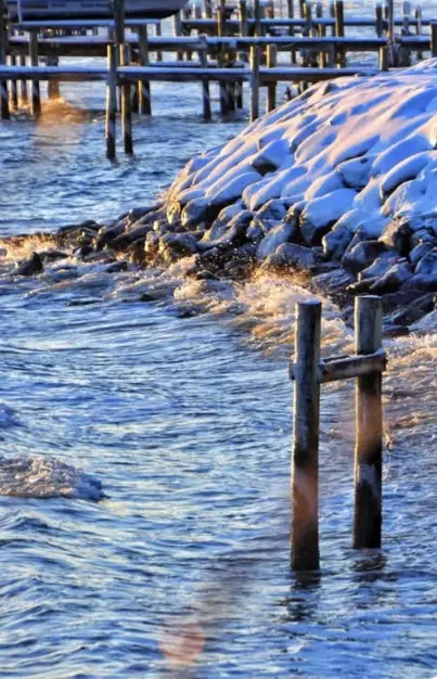 A snowy shoreline with waves crashing against rocks and wooden pilings, overlaid with the text 'i'm not a snowflake i'm a…