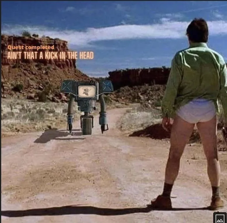 A man in a green shirt and white underwear stands facing a small, TV-headed robot in a desert. Text overlaid in orange reads…