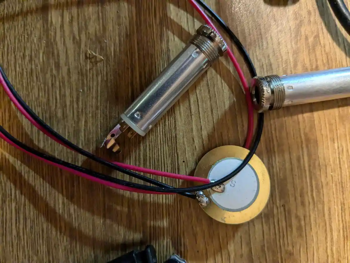 A close-up photo shows electronic components on a wooden surface, including a soldering iron tip, red and black wires, and a…