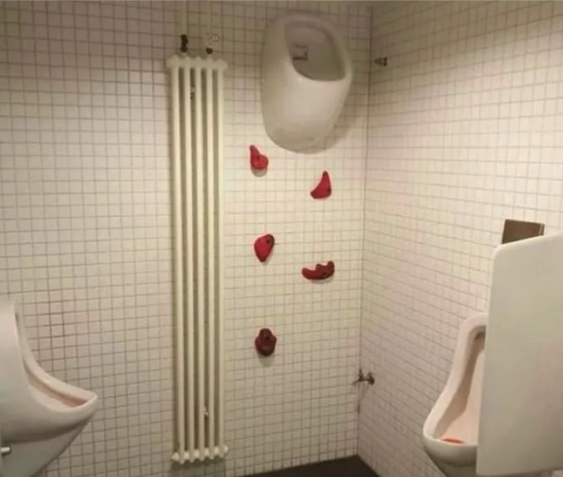 A bathroom stall with white tiled walls features a urinal mounted on the wall above a radiator, with several red…