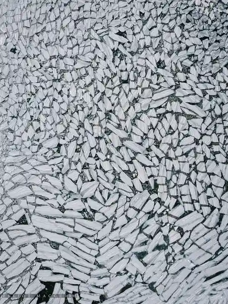 An aerial photograph shows a dense field of shattered ice floes floating on dark water, creating a fragmented, textured…