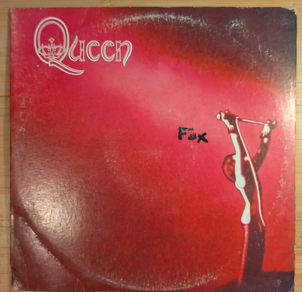 A worn, red Queen album cover featuring the band's logo and a stylized figure holding a microphone, with the word 'Fox'…