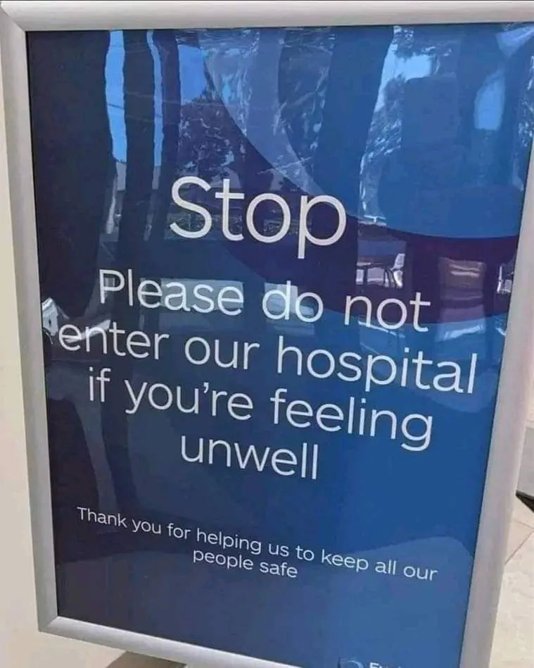 A blue hospital sign with white text reads 'Stop Please do not enter our hospital if you're feeling unwell Thank you for…