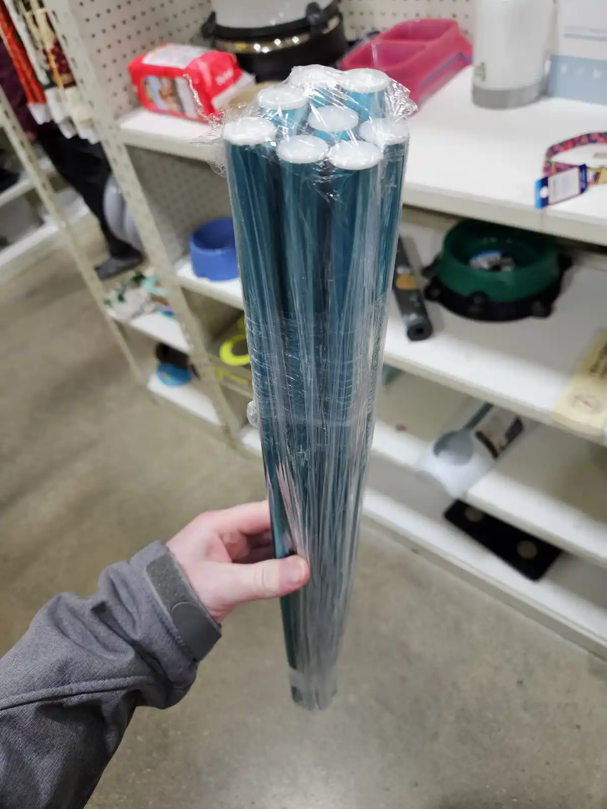 A person's hand holds a large bundle of teal-colored plastic sticks wrapped in clear plastic, resembling a torch or candle…