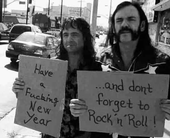 Two men with long hair and beards stand on a street holding handmade signs. The man on the left holds a sign that reads…