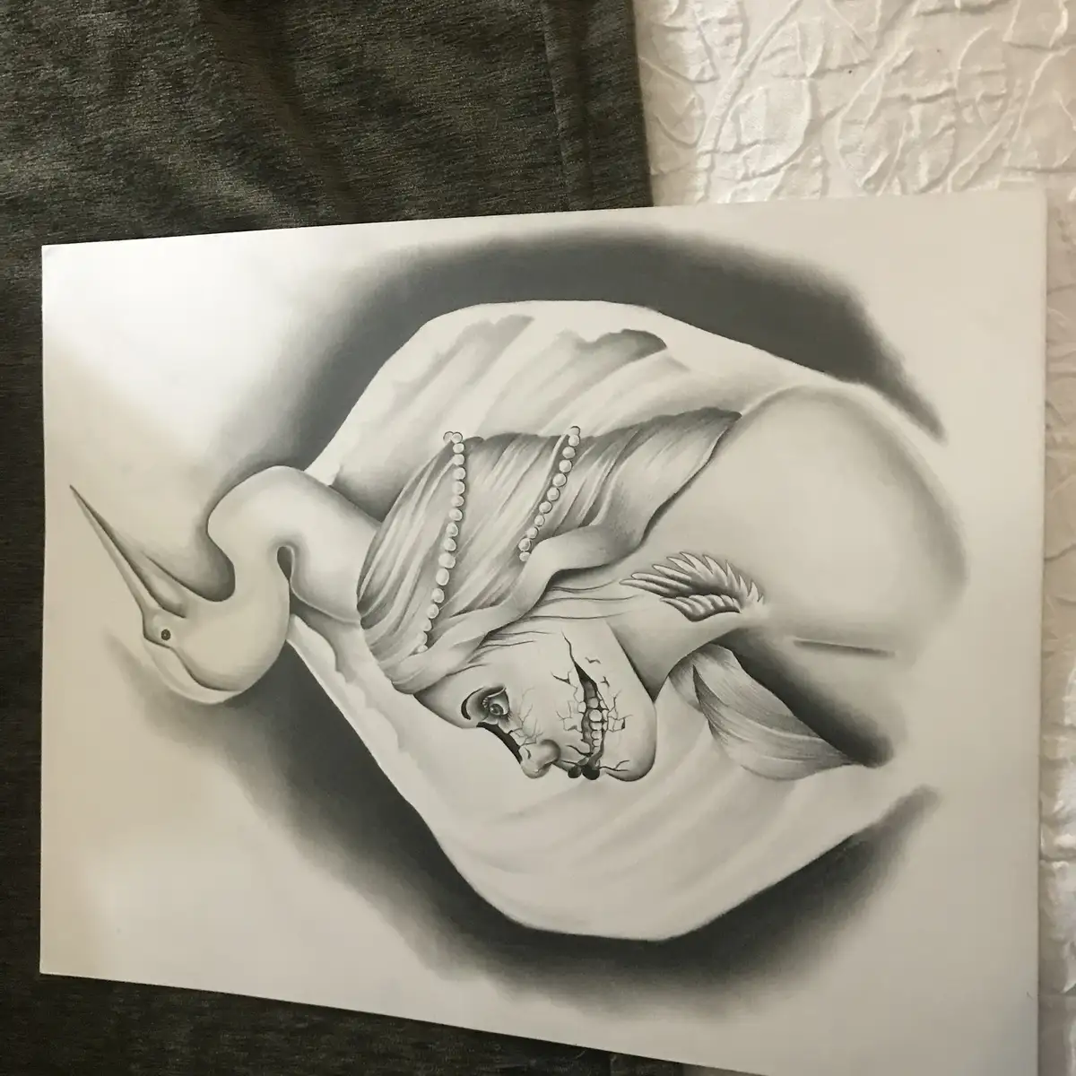 A black-and-white pencil drawing shows a woman with a cracked, skeletal face and pearl necklace, her head resting inside a…