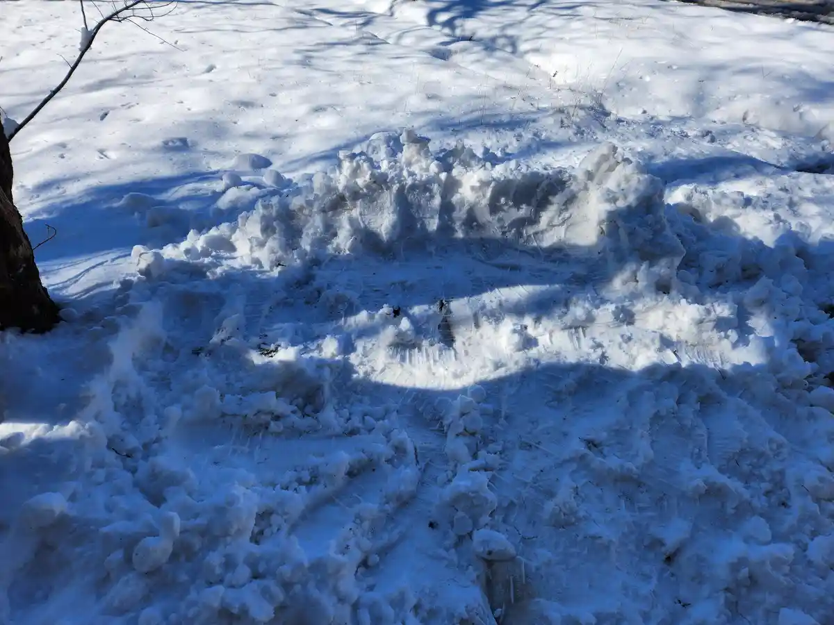 A snowy outdoor scene shows a snow angel made by someone lying on their back, with wings spread, leaving distinct…