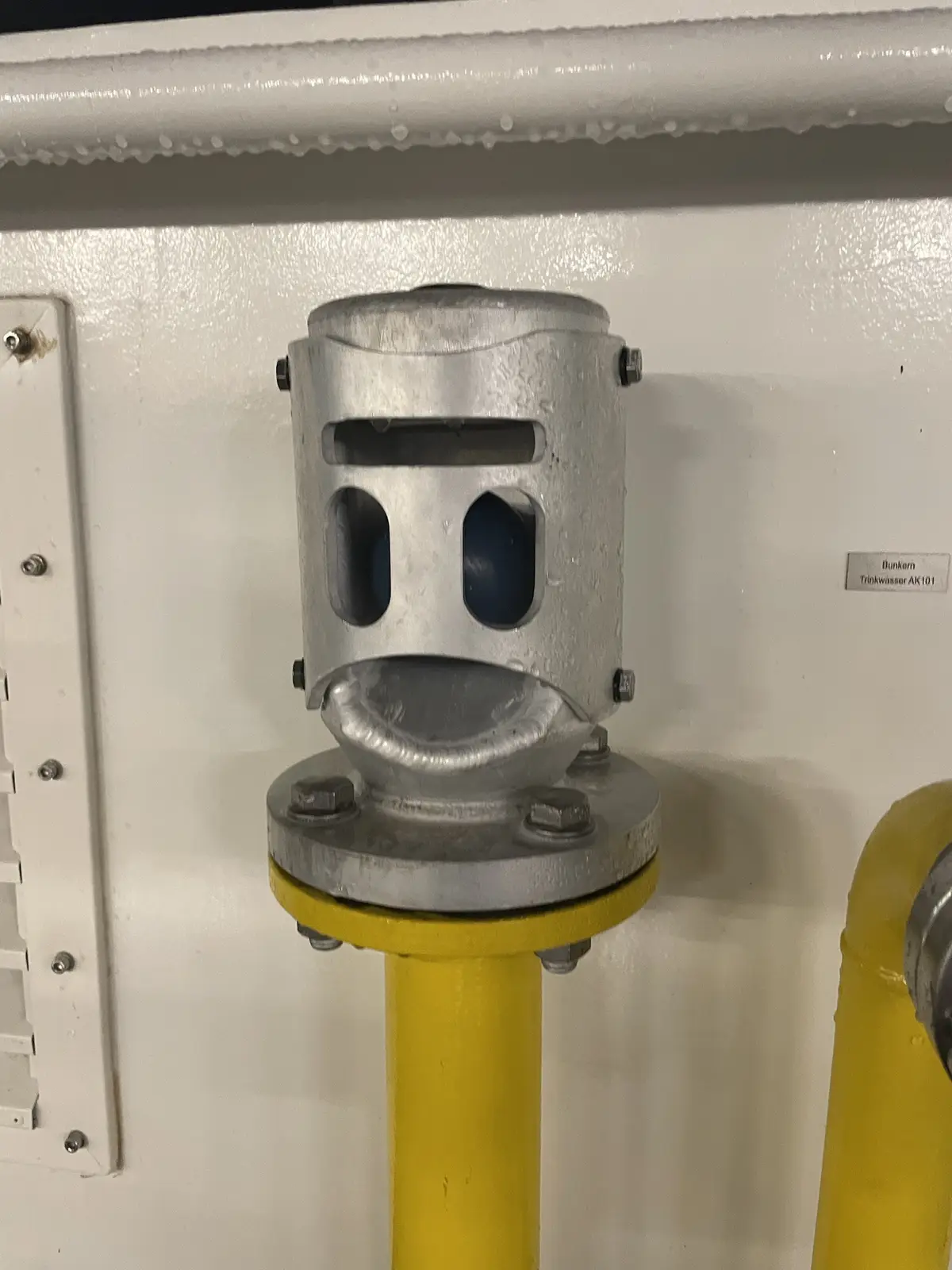A close-up photo of a silver industrial pipe fitting mounted on a yellow pipe, which has been humorously edited to resemble…