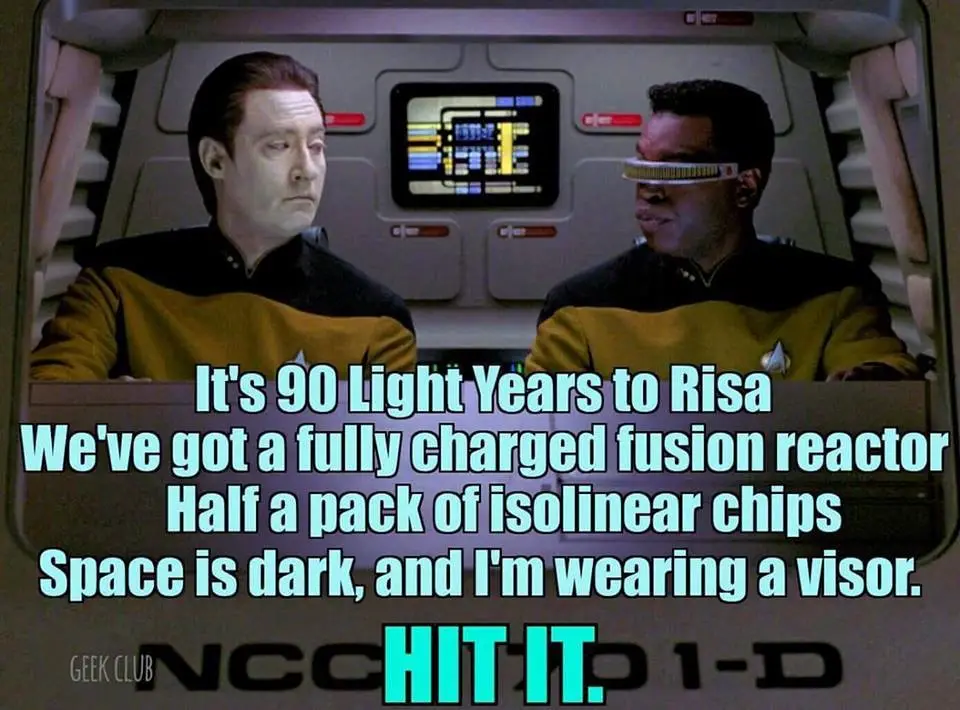 Two men in Starfleet uniforms sit in a spaceship cockpit. The man on the right wears a visor and speaks while the man on the…