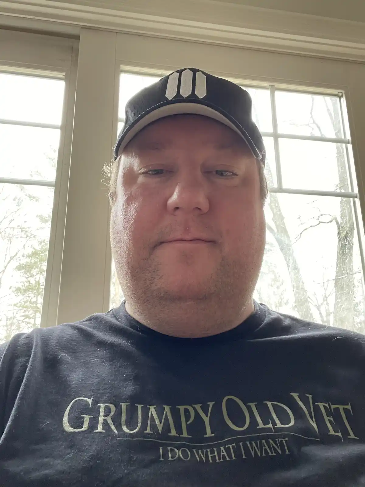 A man with a neutral, slightly grumpy expression wears a dark t-shirt with the text 'GRUMPY OLD VET I DO WHAT I WANT'…