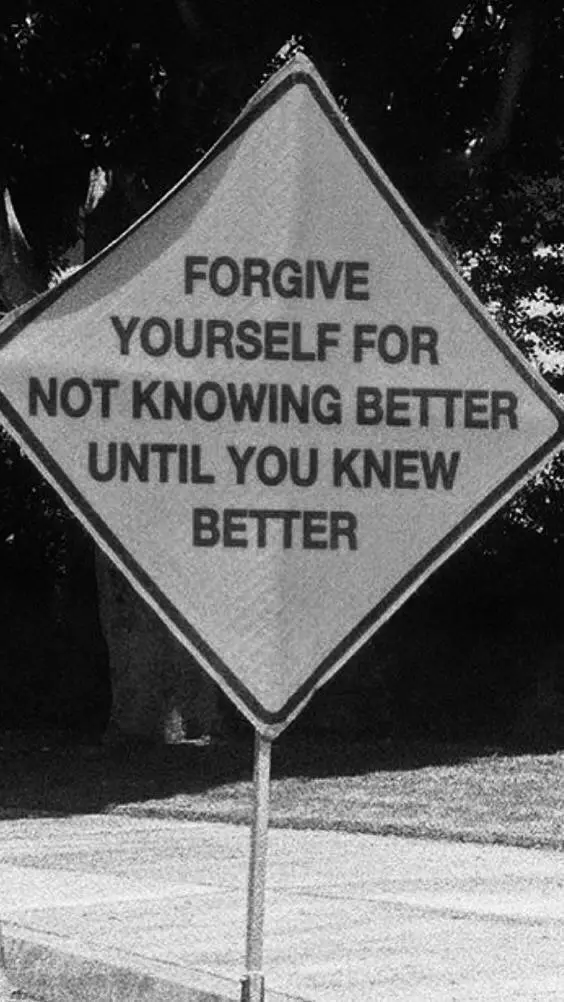 A black-and-white photo of a diamond-shaped road sign with bold, centered text that reads 'FORGIVE YOURSELF FOR NOT KNOWING…