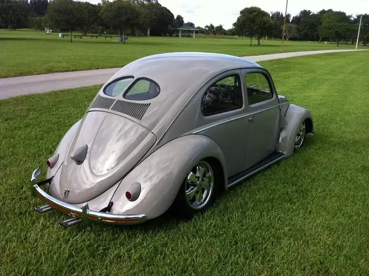 a silver custom volkswagen beetle with a lowered suspension, custom chrome wheels, and a modified rear bumper is parked on a…