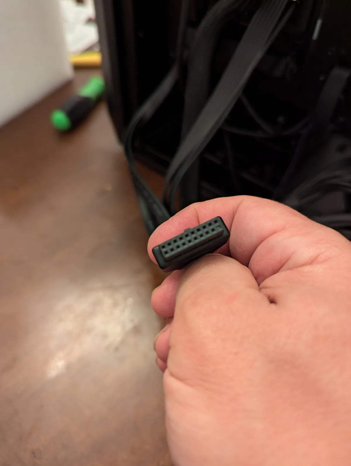 A close-up photo shows a person's hand holding a small, black, rectangular multi-pin computer cable connector. In the…