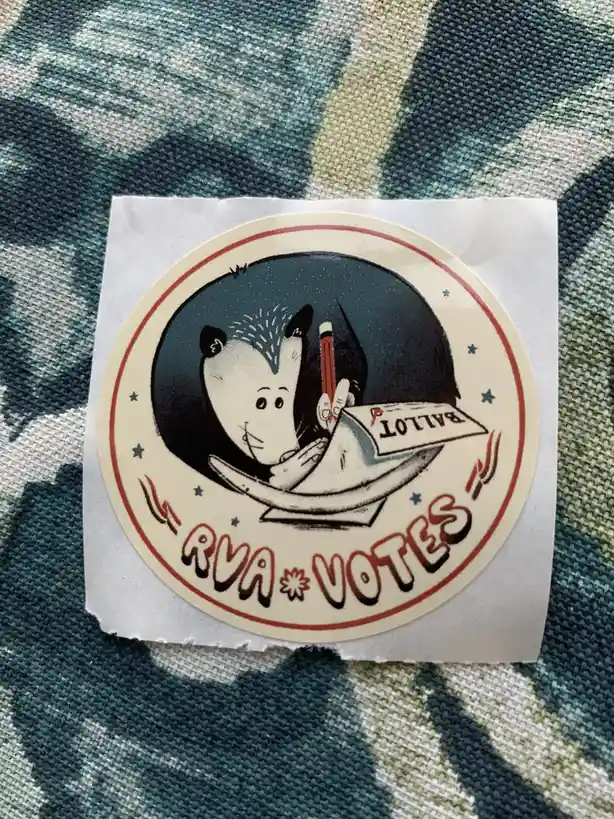 A circular sticker features a cartoon opossum holding a pencil and a ballot paper labeled 'BALLOT' against a dark background…