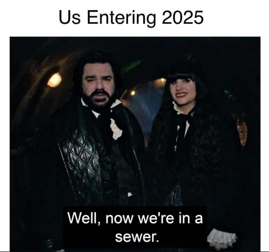A still image from a movie shows two characters, a man with a beard and a woman with dark hair, standing in a dimly lit…