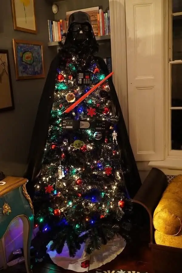 A decorated christmas tree is draped with a full-sized darth vader costume, including his helmet and cape, with a red…