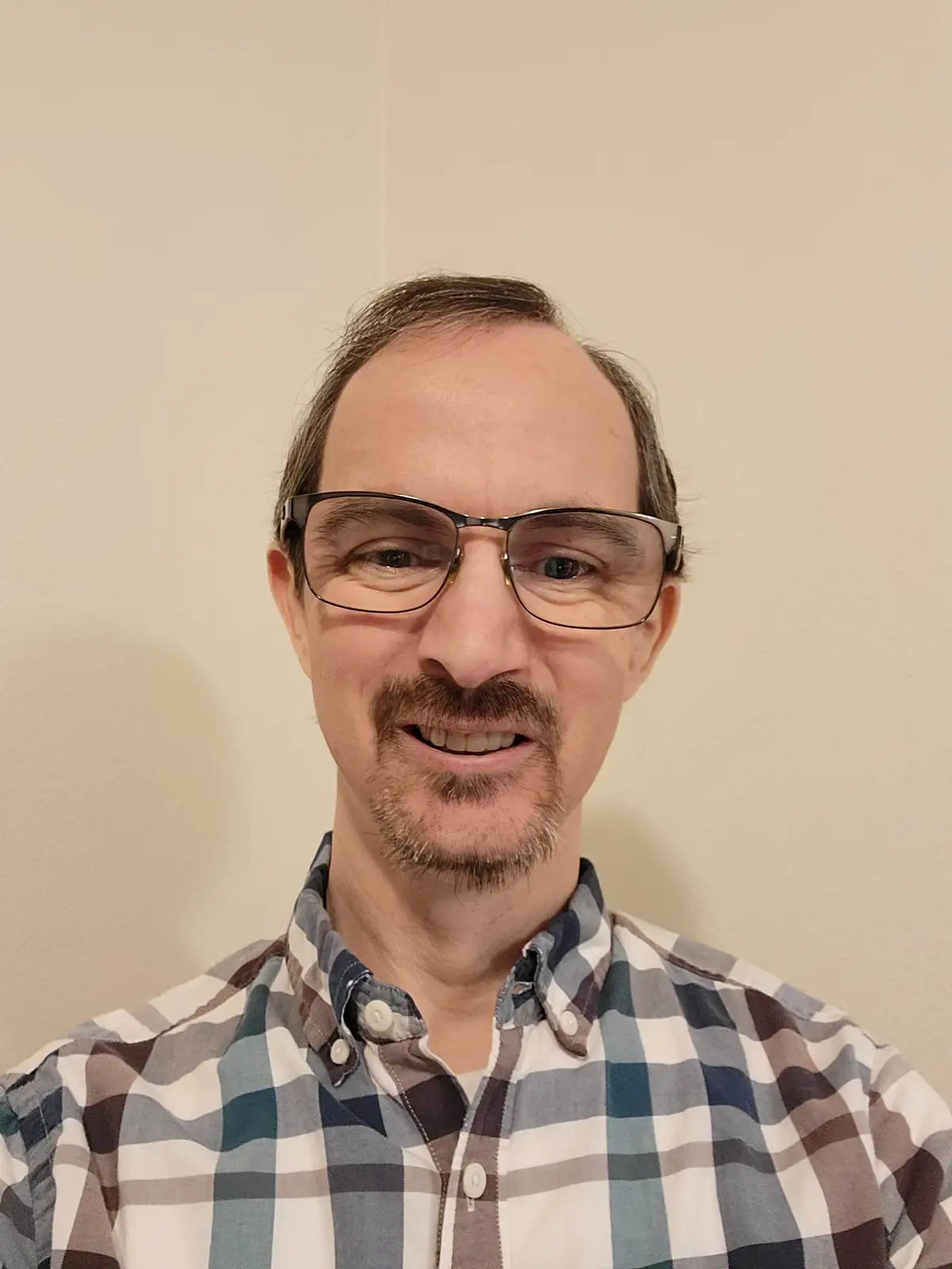 A middle-aged man with glasses and a mustache smiles at the camera while wearing a plaid shirt, with the text 'i'm not a fan…