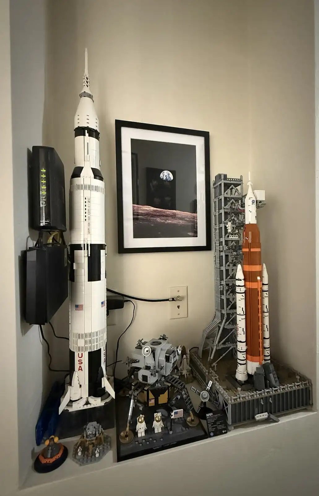 A shelf displays several large LEGO space models including a Saturn V rocket, an Apollo lunar module, and a Space Launch…