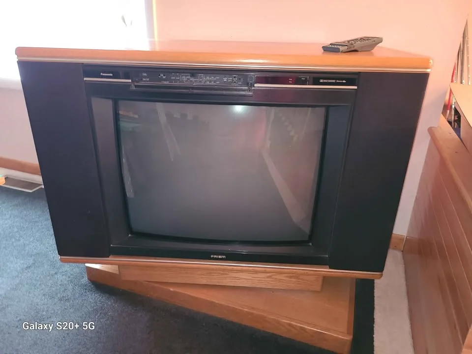 A vintage 1980s-style CRT television with a wooden casing and black plastic frame sits on a wooden stand in a room. The…