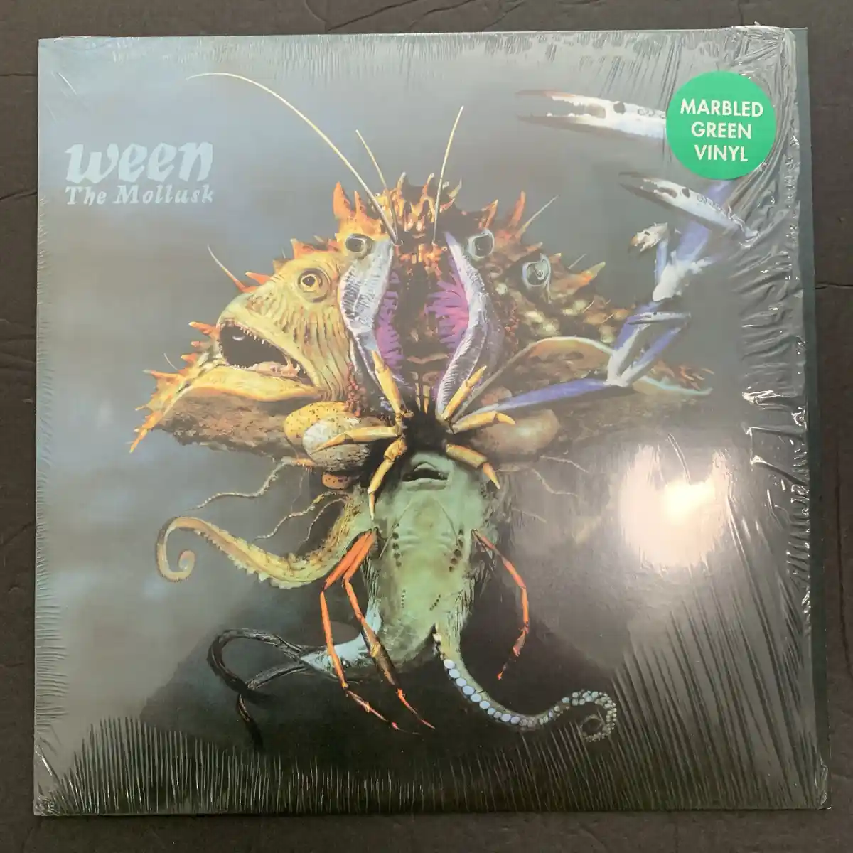 A sealed vinyl record album cover for Ween's 'The Mollusk' features a surreal, grotesque collage of sea creatures including…