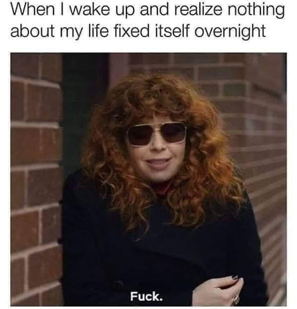 A woman with curly red hair and sunglasses stands against a brick wall, looking slightly exasperated. The text above her…