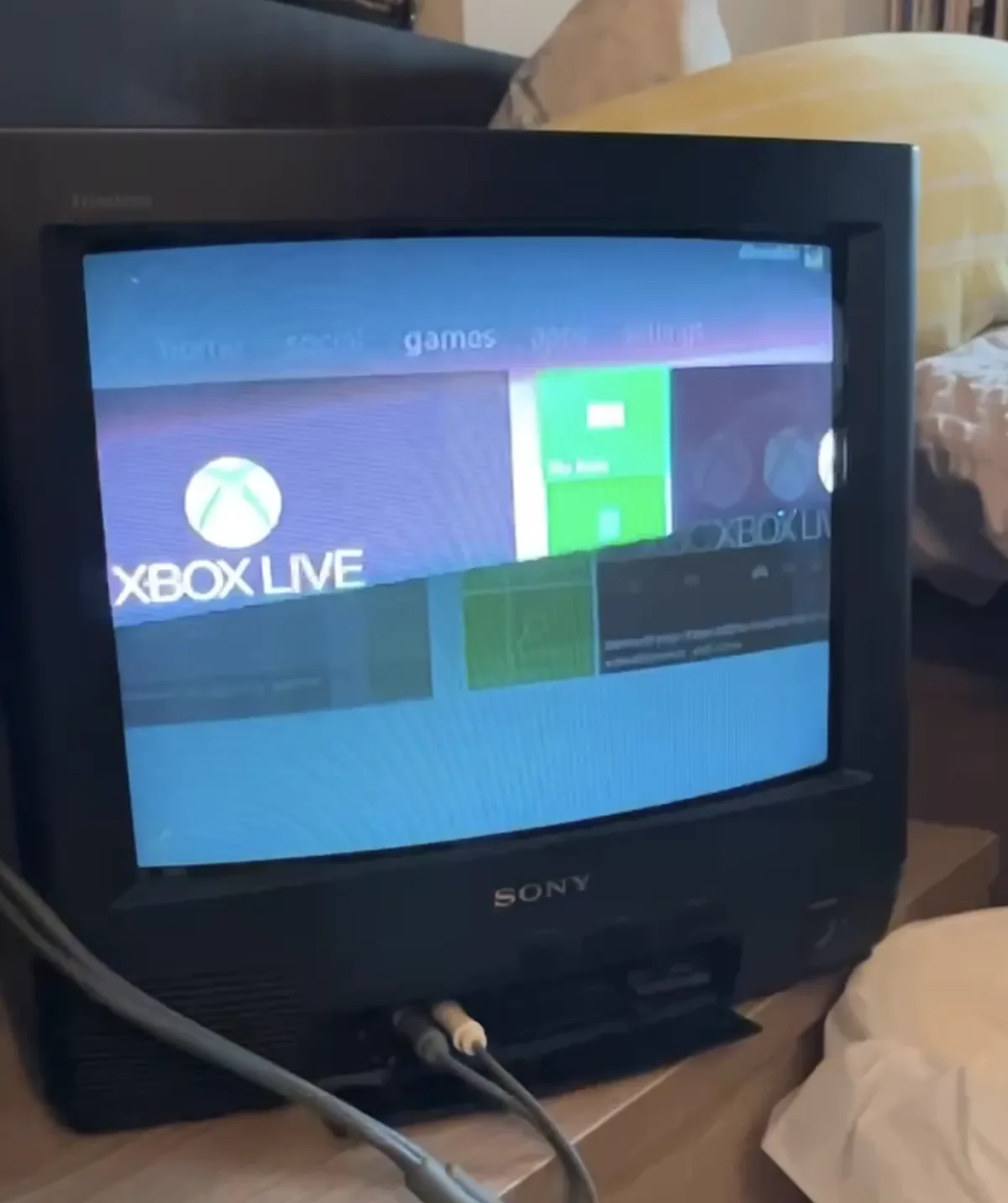 A vintage Sony Trinitron CRT television displays the Xbox Live dashboard interface, featuring the Xbox logo and menu options…