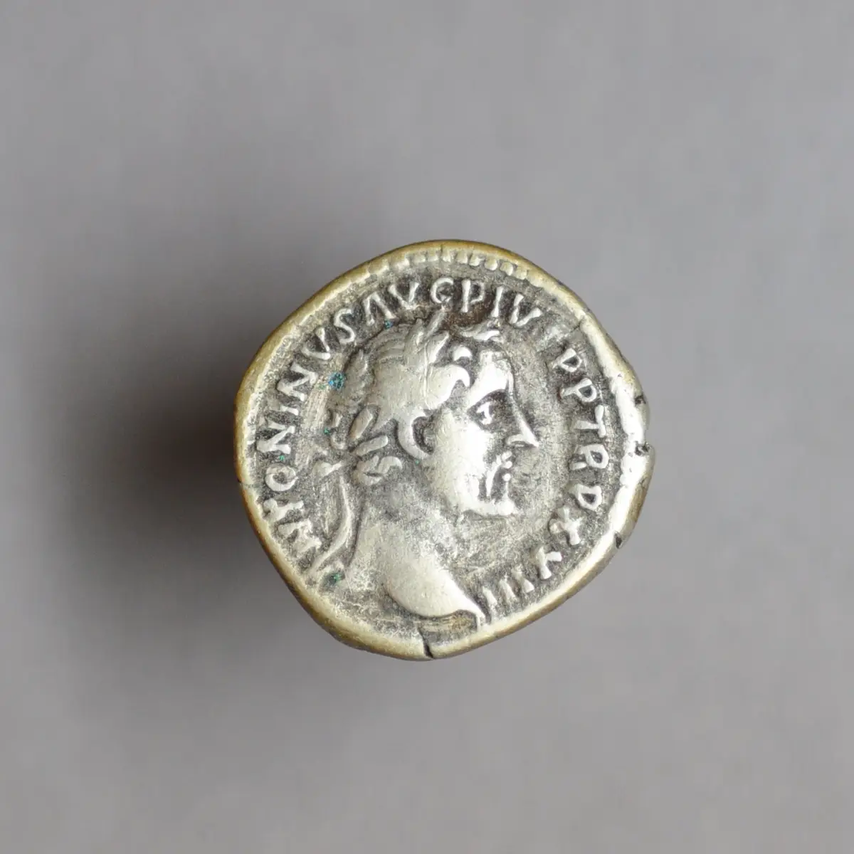 A close-up photograph of an ancient, worn Roman silver coin featuring a profile bust of a man, likely Marcus Aurelius, with…