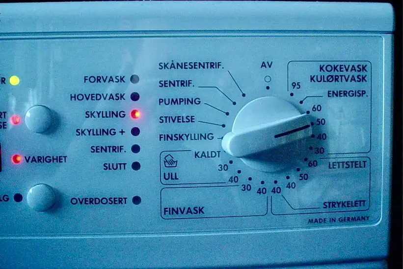 A close-up of a washing machine control panel with a large dial set to 'AV' (off), while several indicator lights are…